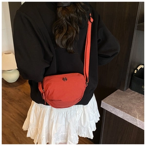 Detail of a brick-red nylon crescent shoulder bag with adjustable strap on a model