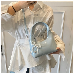 Light blue half-moon handbag with pearl bow pendant worn by model in minimalist setting