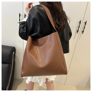 Détail du sac cabas tressé caramel porté à l'épaule dans un décor minimaliste