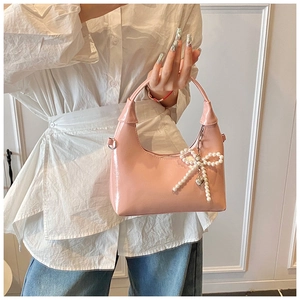 Detail of light pink patent leather handbag with pearl bow and metal heart charm