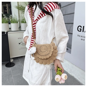 Detail of handwoven straw saddle bag featuring scallop edges and a plush cloud charm