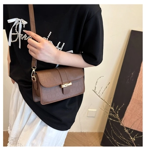 Detail of a brown crocodile pattern crossbody bag featuring a golden twist lock closure
