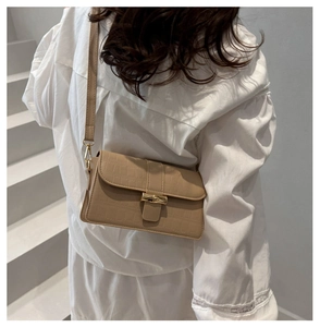 Close-up of beige crocodile pattern handbag featuring a gold bamboo-shaped buckle on strap