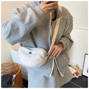 Close-up of cream white nylon crossbody bag with wide strap worn on grey sweatshirt