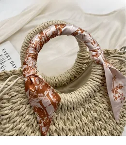 Detail view of woven straw tote with floral silk scarf wrapped around circular handles