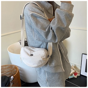 Detail of cream half-moon crossbody bag on a grey hoodie, featuring round metal logo
