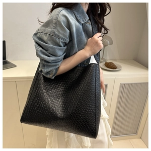 Détail d'un grand sac cabas noir à texture tressée porté à l'épaule dans un décor urbain