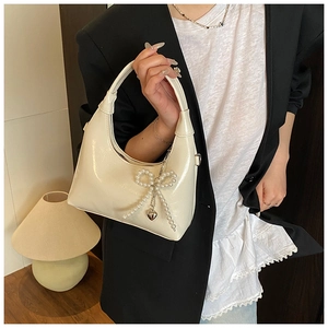 Close-up of glossy cream white shoulder bag with pearl bow and silver heart pendant