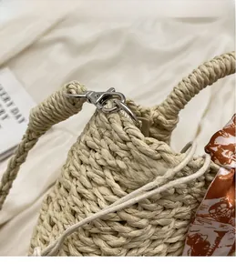 Detail of woven straw handbag featuring silver metal hooks and artistic print silk scarf
