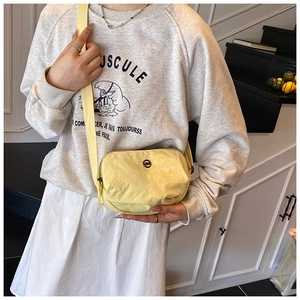 Close-up of bright yellow nylon crossbody bag with black circular metal logo detail