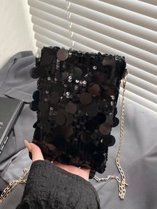 Chic black sequin tote bag with gold chain strap held against a neutral background