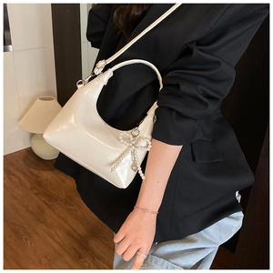 Close-up of white crescent bag with pearl bow charm and adjustable shoulder strap