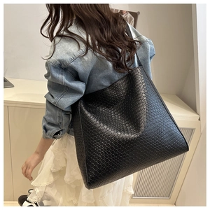 Détail d'un grand sac cabas en cuir tressé noir porté par un mannequin en jean