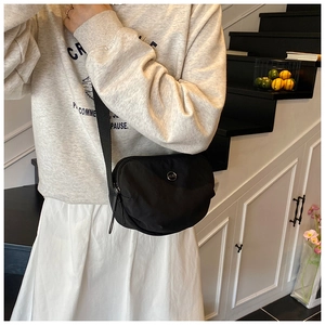 Detail of a black half-moon crossbody bag with silver logo and wide fabric strap