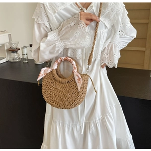 Detail of hand-woven straw bag with floral scarf handle on white lace dress