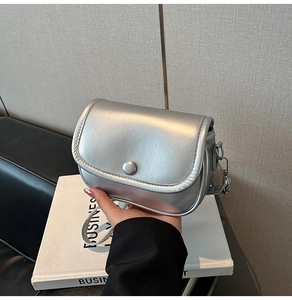 Close-up of a silver metallic crossbody bag with a magnetic round buckle and flap design