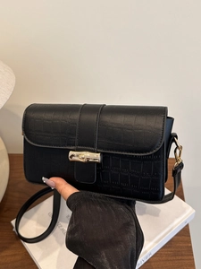 Elegant black crocodile pattern leather crossbody bag with gold bamboo clasp shown in a lifestyle setting