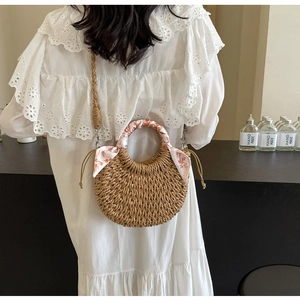 Detail of woven straw crescent bag with drawstring closure and floral scarf on handle