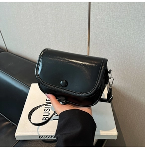 Glossy black patent leather mini crossbody bag with round button closure and adjustable strap