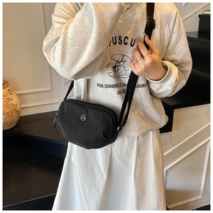 Detail view of a compact black nylon crossbody bag with adjustable strap and metal logo