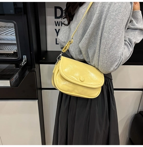 Detail of yellow patent leather crossbody bag with glossy finish and pleated texture