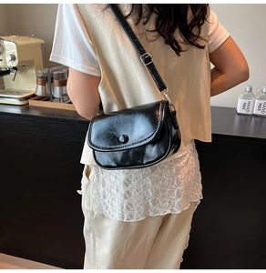 Detail of a vintage black oiled leather crossbody bag on a modern cafe background