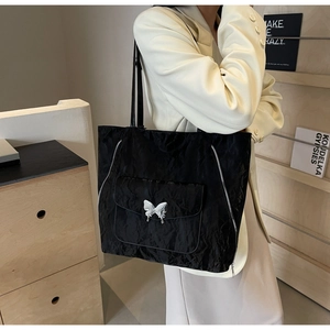 Detail of black tote bag featuring textured fabric and silver butterfly buckle on shoulder