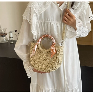 Detail of half-moon straw bag with floral scarf accent and woven strap for crossbody wear