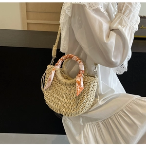 Detail of woven straw crossbody bag with orange patterned silk scarf handle and lace dress