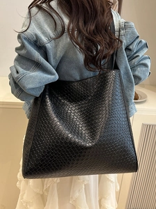Grand sac cabas noir tissé porté par un mannequin, style seau chic et minimaliste