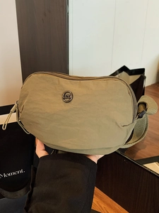 Olive green crescent nylon crossbody bag with wide strap and circular logo detail
