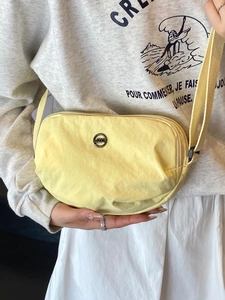 Minimalist light yellow nylon crossbody bag featuring round metal logo and adjustable strap