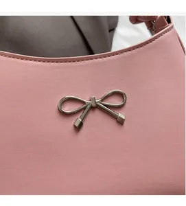 Detail of light pink leather shoulder bag featuring a silver metal bow ornament and fine stitching