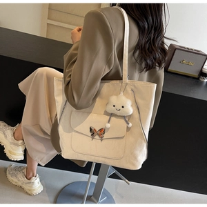 Detail of minimalist cream tote bag with butterfly buckle pocket and plush cloud charm
