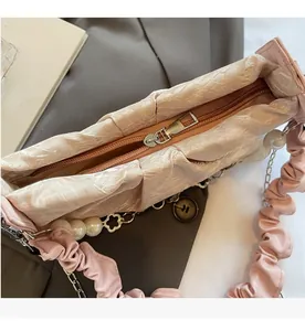 Close-up of a pink pleated cloud bag featuring smooth silver zipper and pearl chain detail