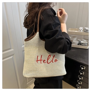 Detail of hand-woven straw tote bag with red Hello embroidery and brown leather strap