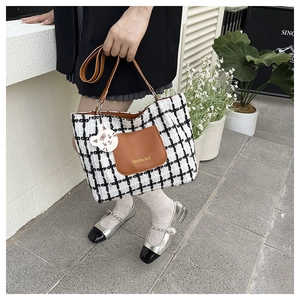 Dettaglio della borsa tote in tweed a scacchi con tasca in pelle e ciondolo gatto