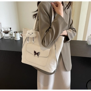Close-up of cream canvas tote bag with butterfly buckle and cloud pendant on casual shoulder strap