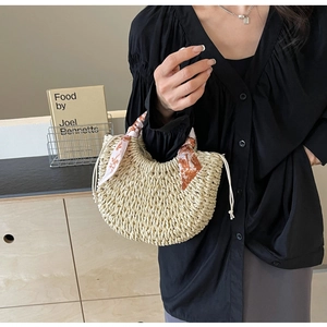 Detail of woven straw moon bag featuring geometric silk scarf wrapped on the handle