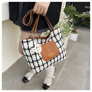 Dettaglio della borsa tote in tweed a quadri con tasca in pelle marrone e ciondolo gatto
