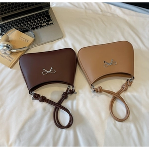 Close-up of minimalist leather handbags featuring knotted straps and silver bow charms
