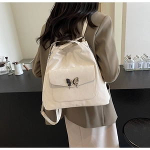 Detail of cream backpack showing textured faux leather and butterfly metal clasp on model
