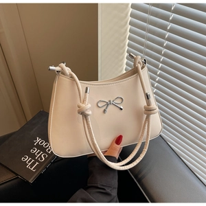 Detail of beige shoulder bag with metal bow accent and twisted braided handle