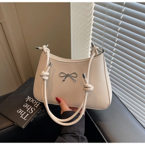 Detail of cream shoulder bag featuring a silver metal bow and knotted strap design