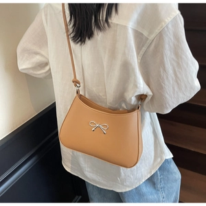 Detail of camel brown faux leather shoulder bag with silver bow accent on model