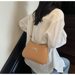 Detail showing a light brown leather shoulder bag with a silver bow on a model outfit