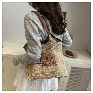 Detailed view of beige woven tote bag with red Hello embroidery and brown leather trim