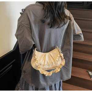 Detail of cream pleated cloud bag with pearl charm and metal chain strap on a model