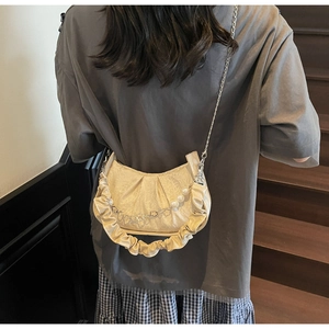 Close-up of creamy pleated cloud bag with pearl chain and metal flower charm detail