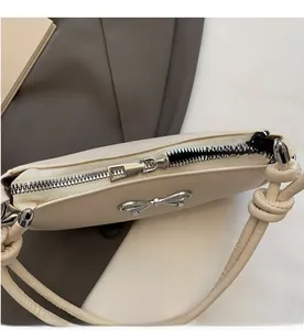 Detail of silver smooth zipper and metallic bow decoration on off-white shoulder bag